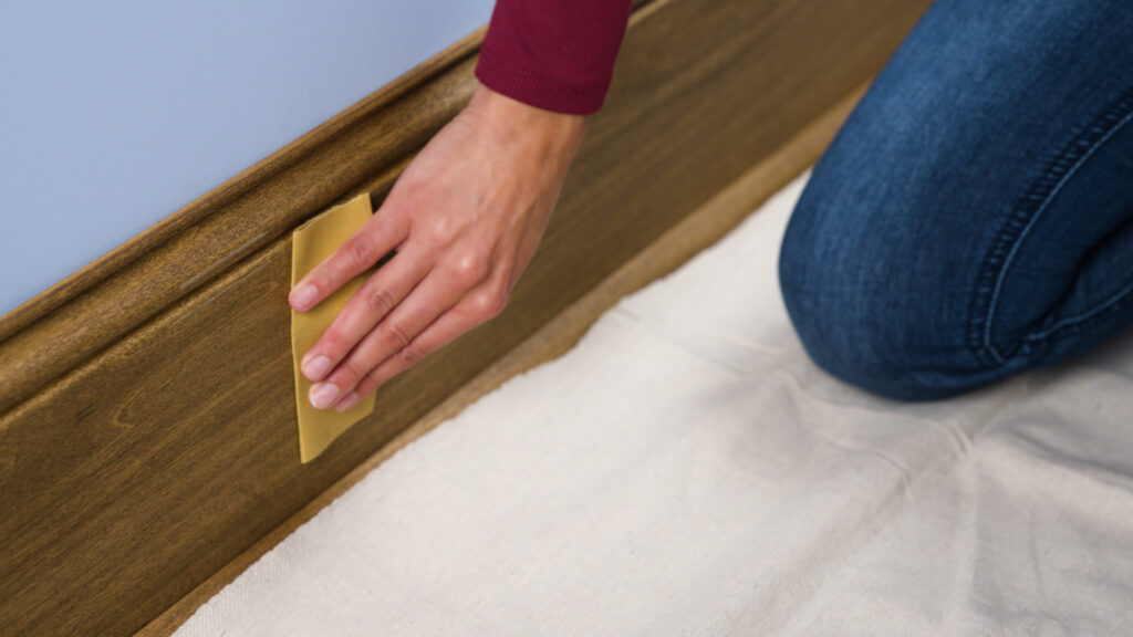 person sanding the trim inside of a house so the paint can stick better